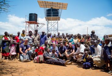 Kenya Community and Team Members Pose Near a Water Tower
